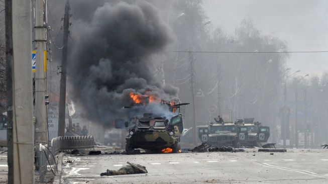 Foto ini menunjukkan sebuah kendaraan pengangkut personel lapis baja Rusia (APC) terbakar di samping tubuh tentara tak dikenal selama pertempuran dengan angkatan bersenjata Ukraina di Kharkiv, Ukraina, Minggu (27/2/2022). [Sergey BOBOK / AFP]